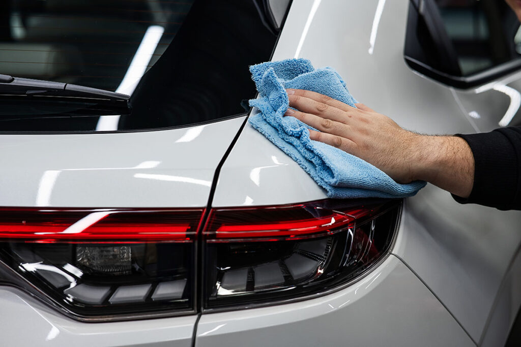 A man is wiping the bumper of a car with a microfiber cloth.