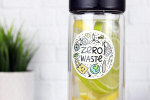 A sticker with the text "Zero Waste" is on a water bottle against a white wall.