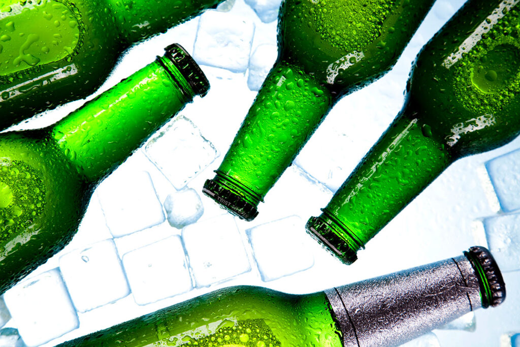 Close-up of several green glass bottles with condensation, arranged on a bed of ice cubes.