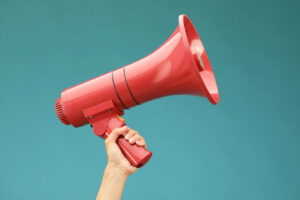 A person holds a bright red megaphone against a turquoise background.