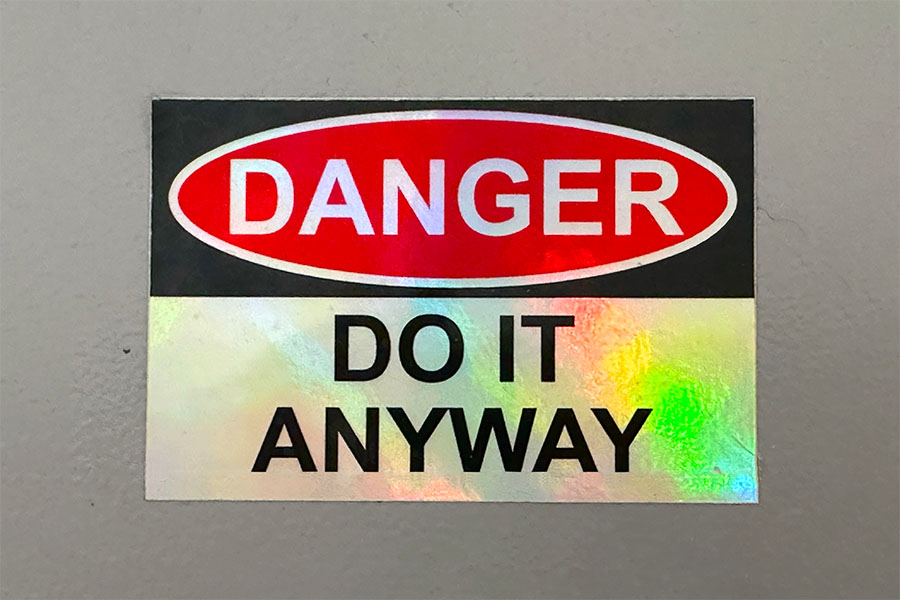 A warning sign that reads "DANGER" in red letters on a black background, with the phrase "DO IT ANYWAY" in bold black letters on a holographic background below.
