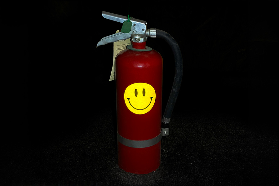 A red fire extinguisher with a yellow smiley face sticker, set against a dark background.